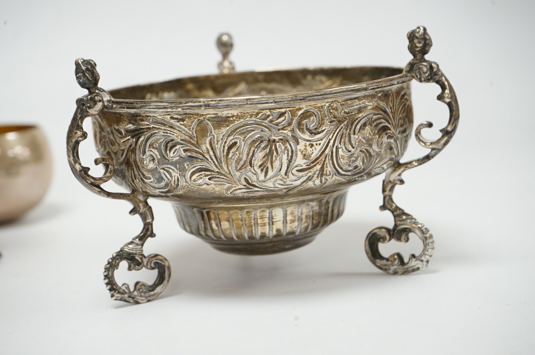 A late Victorian embossed silver bowl, on tripod supports, London, 1890, lacking glass insert?, diameter 12.2cm, together with a Middle Eastern white metal candlestick and a modern silver tumbler cup. Condition - fair to